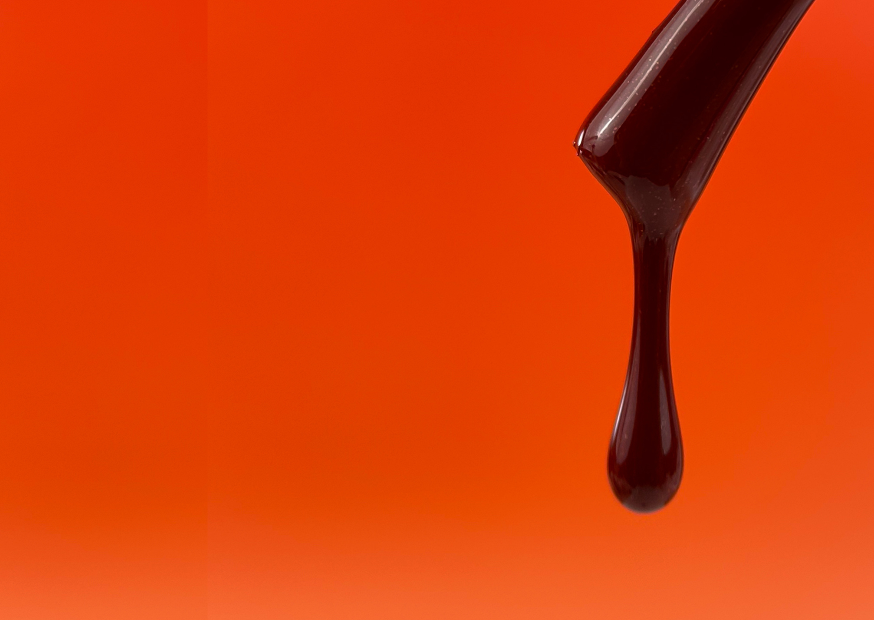 An image of a nail product being dropped from a brush, with orange background